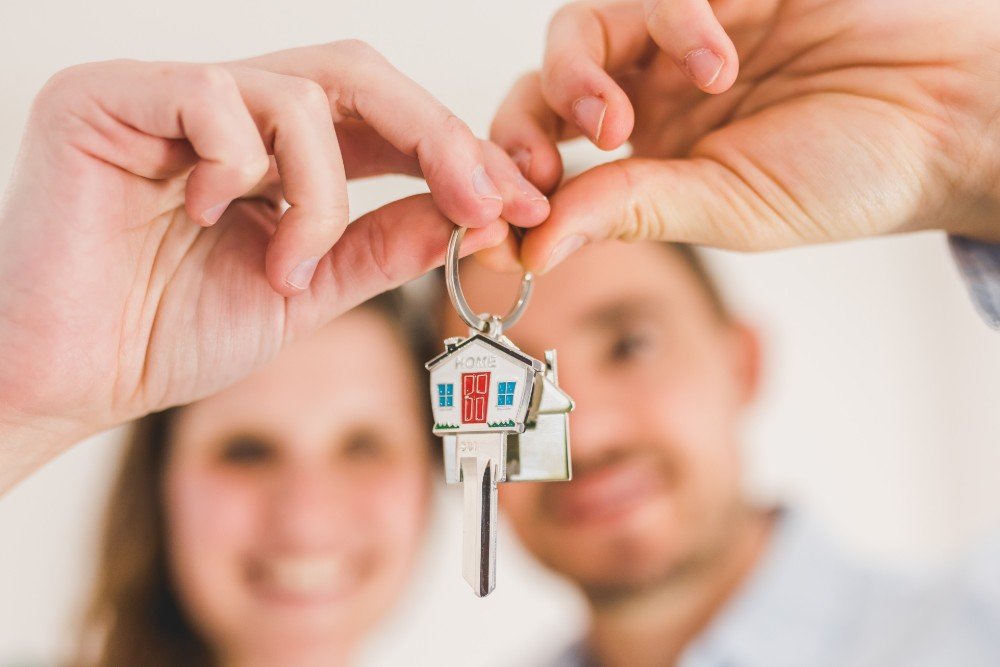 Invertir en bienes raíces, una pareja mostrando las llaves de su nueva casa que consiguieron en una inmobiliaria. 