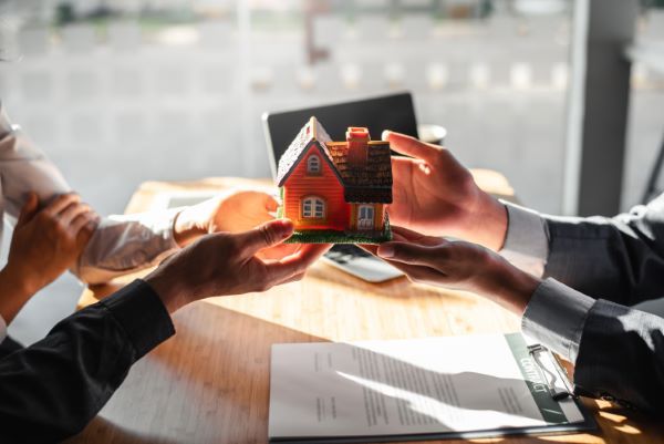 Casas en venta en queretaro; persona entregándole a otra una casa pequeña demuestra