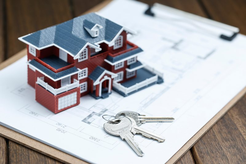 Invertir en bienes raíces, casa miniatura junto a unas llaves sobre un papel con planos