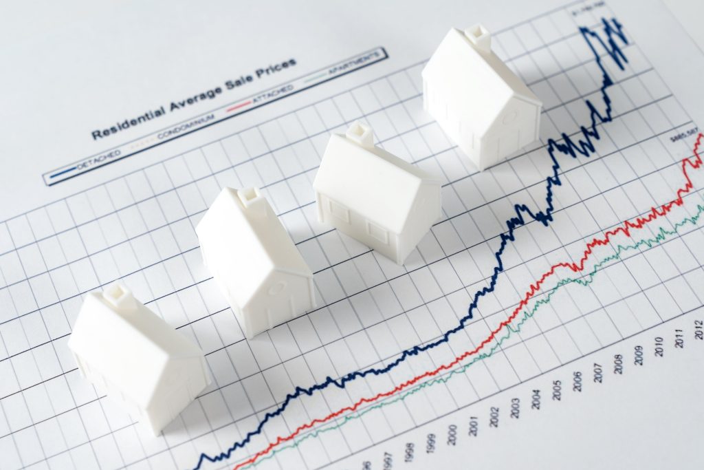 Inversiones inmobiliarias, imagen de tres casas de juguete y una gráfica en aumento en referencia al aumento de la plusvalía de las propiedades. 