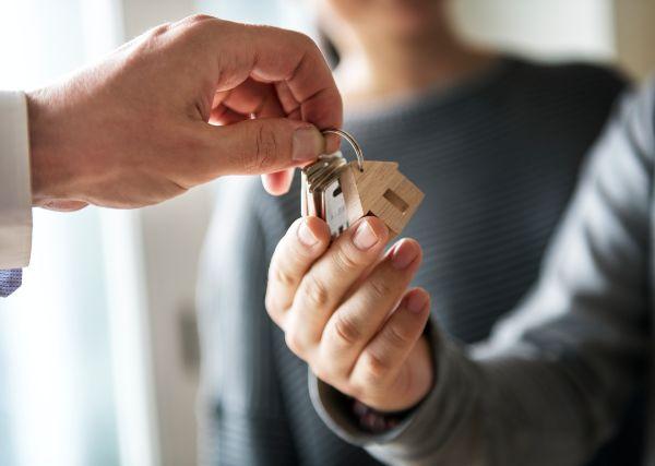 Comprar casa; imagen de detalle mostrando a un asesor de bienes raíces entregando las llaves del nuevo hogar de una pareja.
