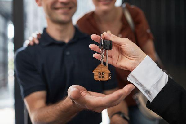 Comprar casa; imagen de un asesor haciendo entrega de unas llaves a una pareja de la compra de su nuevo hogar.
