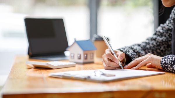 Casas en renta; imagen de un agente inmobiliario revisando papeles para la renta de una propiedad mientras de fondo se ve una pequeña casa de madera.