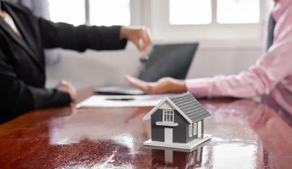 Agente inmobiliario entregando las llaves tras una venta de casas, con el modelo de la propiedad sobre la mesa.