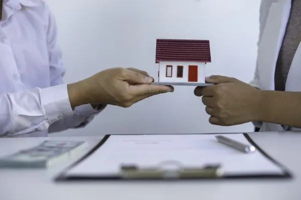 Dos personas en una reunión de corretaje de propiedades, transfiriendo un modelo de casas en venta.