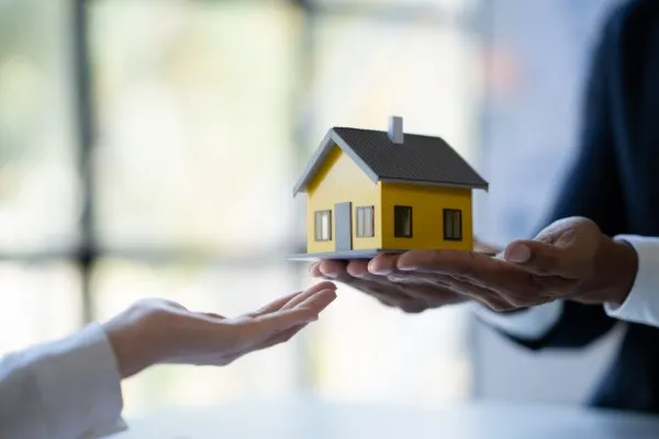 Agente de bienes raíces entregando un modelo de casa a un cliente, simbolizando la compra y venta de casas.